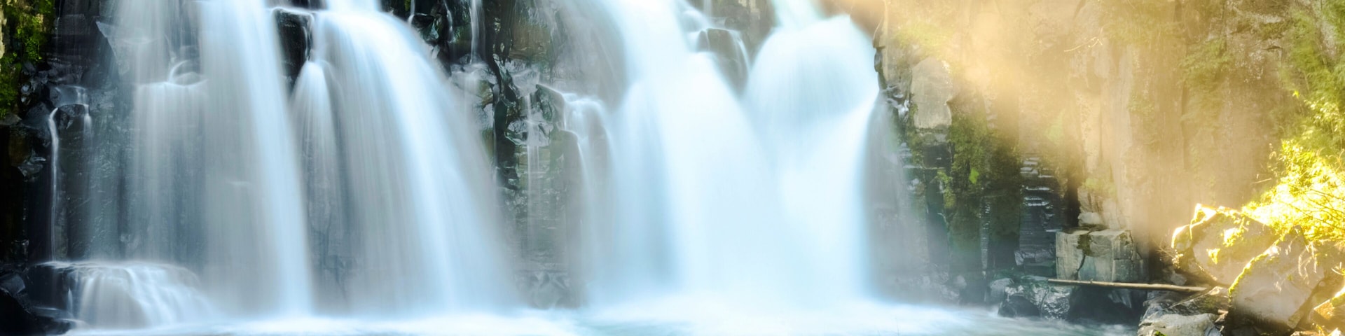 Uma cascata desce sobre rochas em direção a um rio, cercada por vegetação exuberante.
