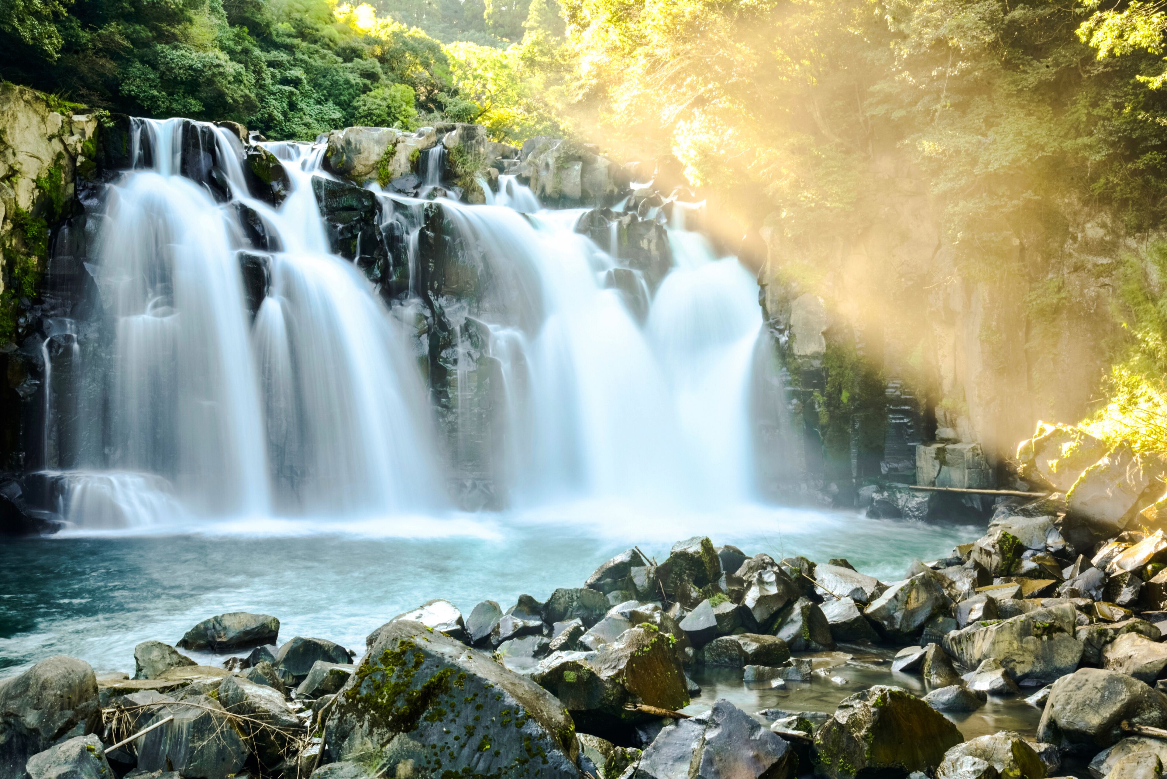 A waterfall cascading over rocks into a river, surrounded by lush greenery.