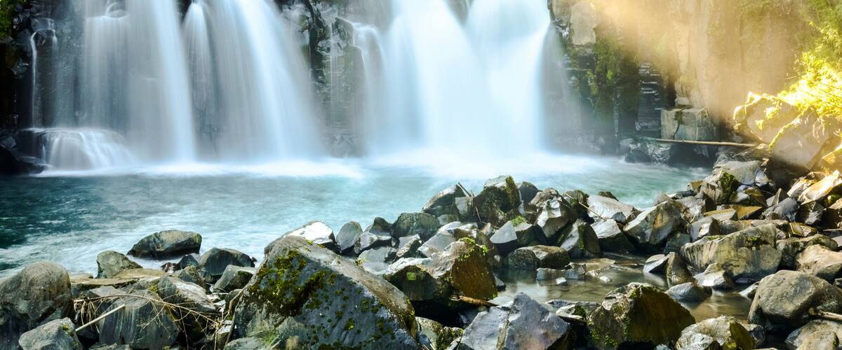 A waterfall cascading over rocks into a river, surrounded by lush greenery.