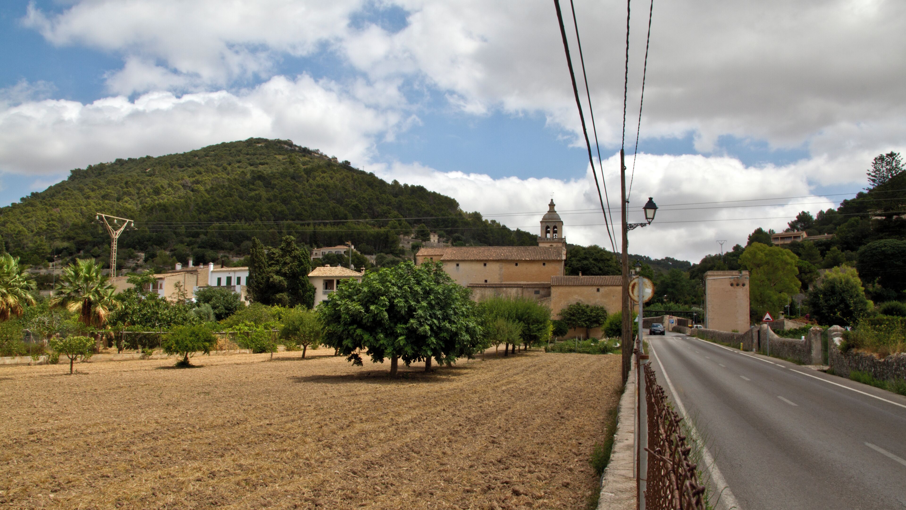 A rural road with a mountain in the background, a church, and a few trees.