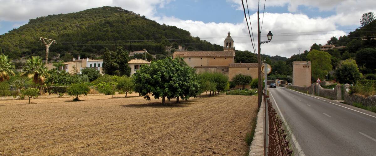 A rural road with a mountain in the background, a church, and a few trees.