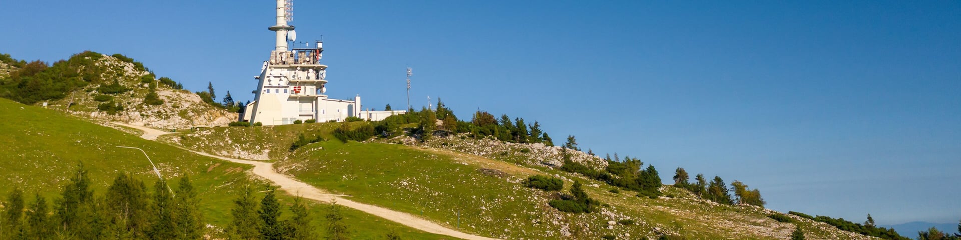 A tall white tower with antennas on a grassy hill under a clear blue sky.