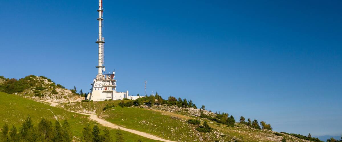 A tall white tower with antennas on a grassy hill under a clear blue sky.