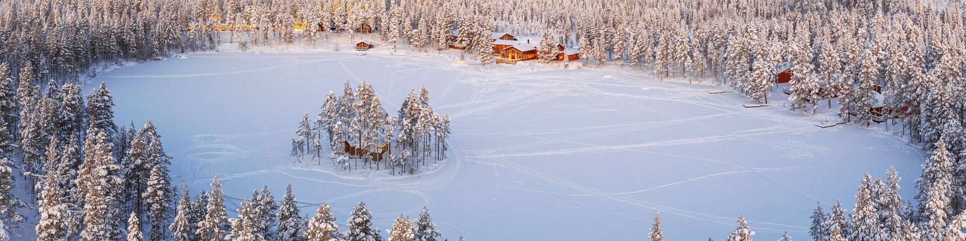 Aerial view of a tourist winter resort in the snow covered forest and the frozen lake in Kangos, Pajala, Norrbotten, Norrland, Lapland, Sweden