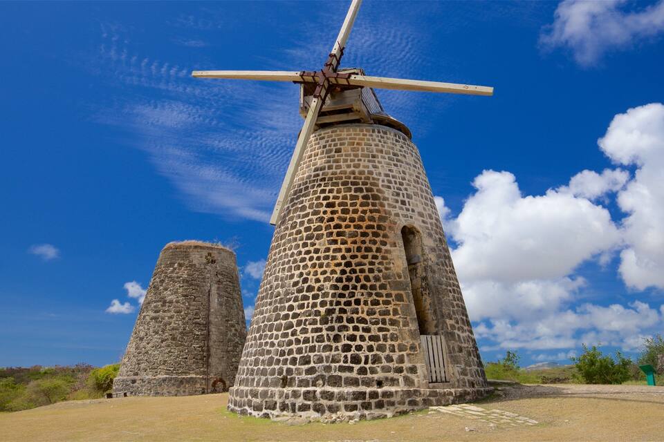 A windmill with a wooden structure and stone base, set against a clear blue sky with scattered clouds.