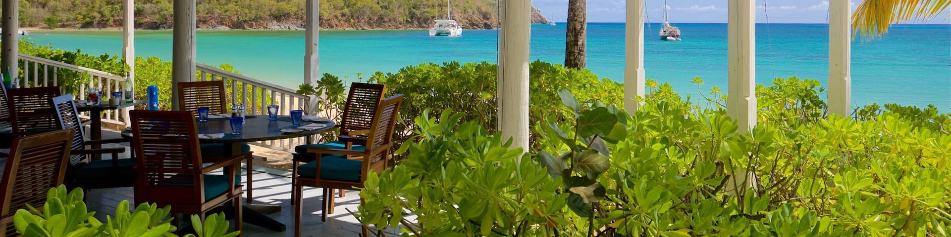 A covered outdoor dining area with a view of turquoise waters and sailboats.