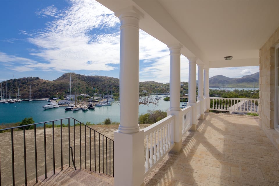 A coastal view with a balcony overlooking a marina, boats, and a mountainous landscape.