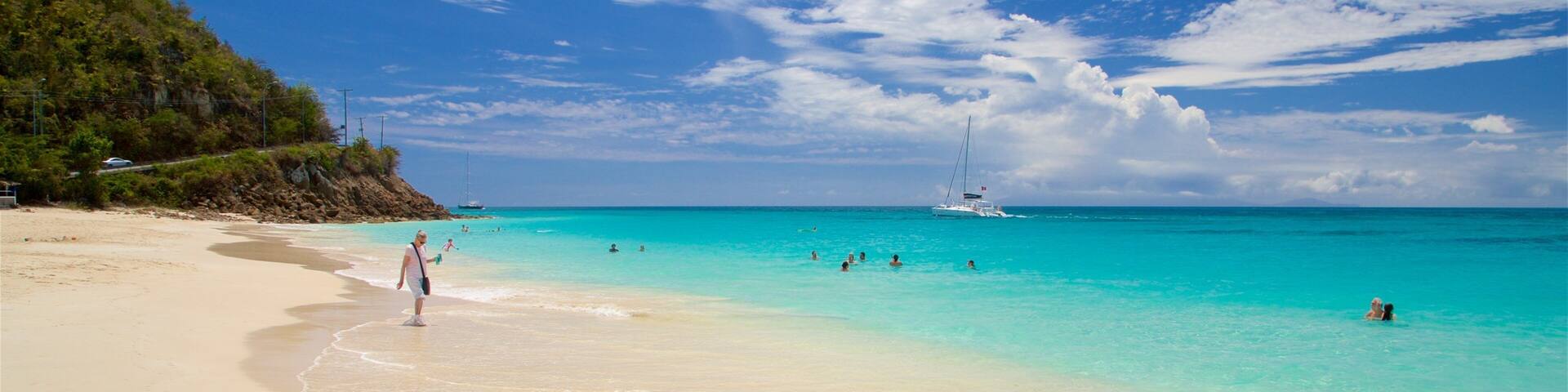 A beach with clear turquoise water, a sandy shore, and a sailboat in the distance.