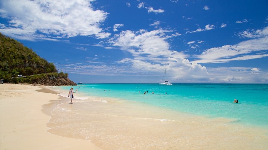 A beach with clear turquoise water, a sandy shore, and a sailboat in the distance.