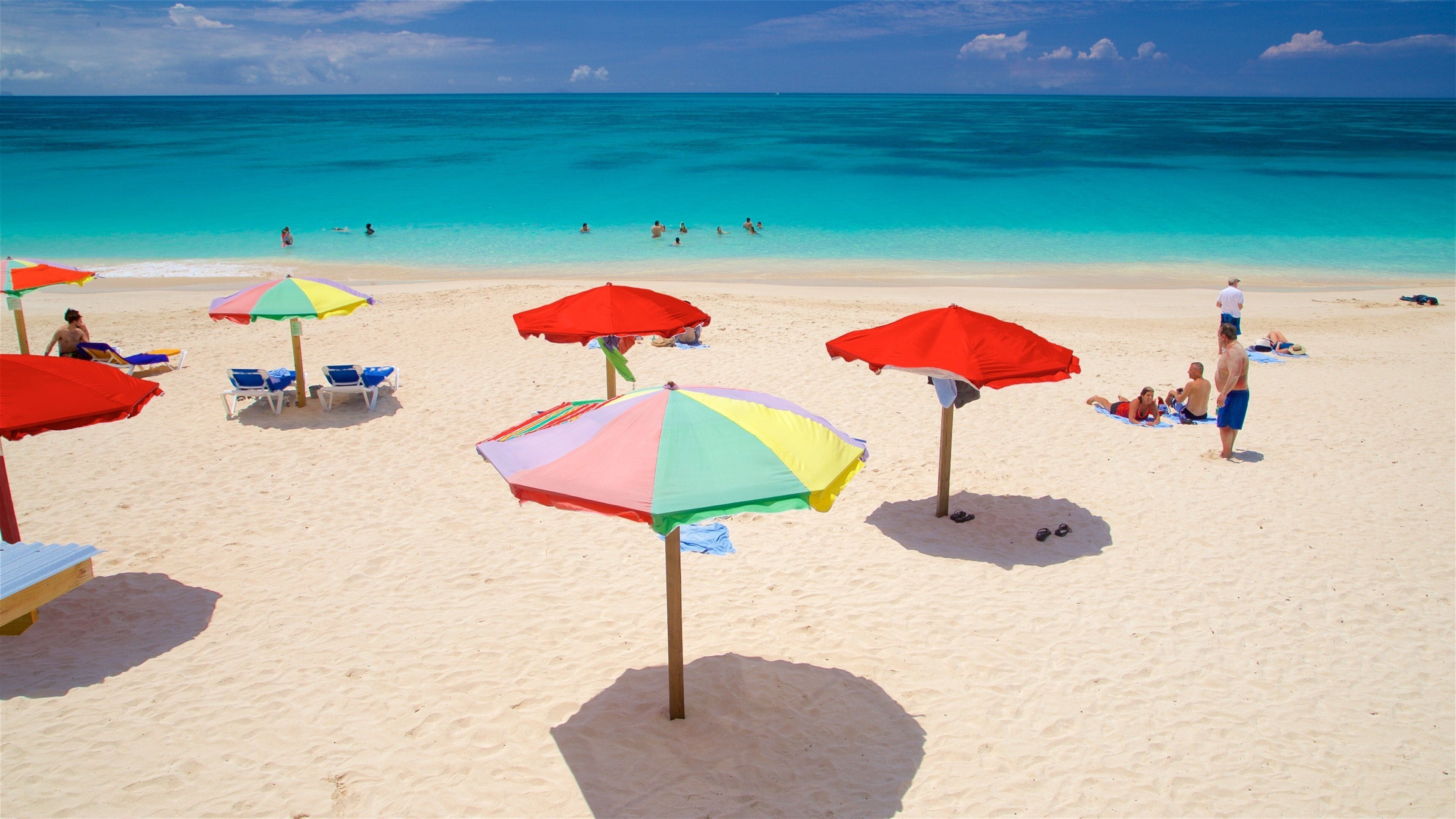 Ein Strand mit bunten Sonnenschirmen, klarem türkisblauem Wasser und sonnenbadenden Menschen.