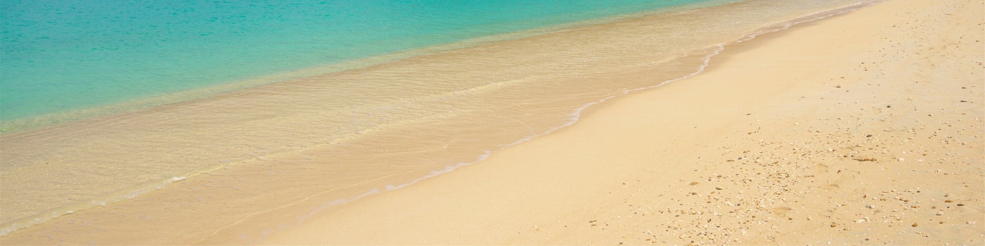 A beach with clear turquoise water, a sandy shore, and a small hill with sparse vegetation.