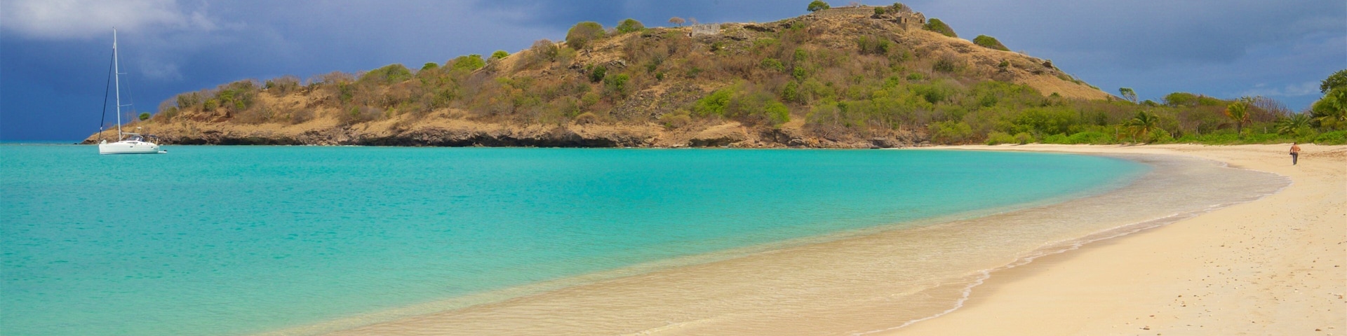 Una playa con agua turquesa cristalina, una orilla arenosa y una pequeña colina con vegetación escasa.