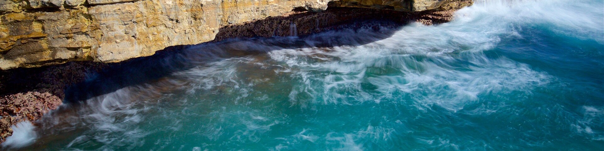 A coastal rock formation with a waterfall and turquoise waters.