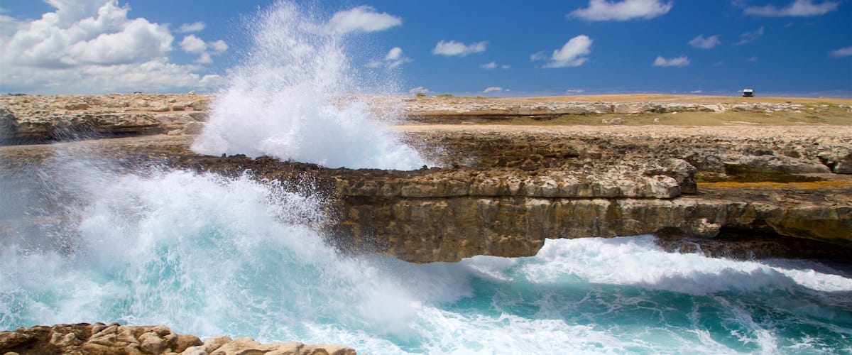 Uma paisagem costeira com ondas quebrando em um afloramento rochoso.