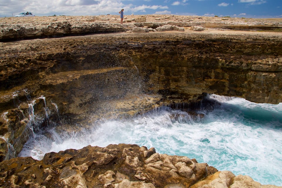 A rocky coastal landscape with a waterfall and ocean waves crashing against the rocks.
