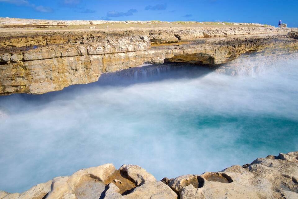 Een kustlandschap met een waterval die in een poel stort, omringd door rotsachtige kliffen.
