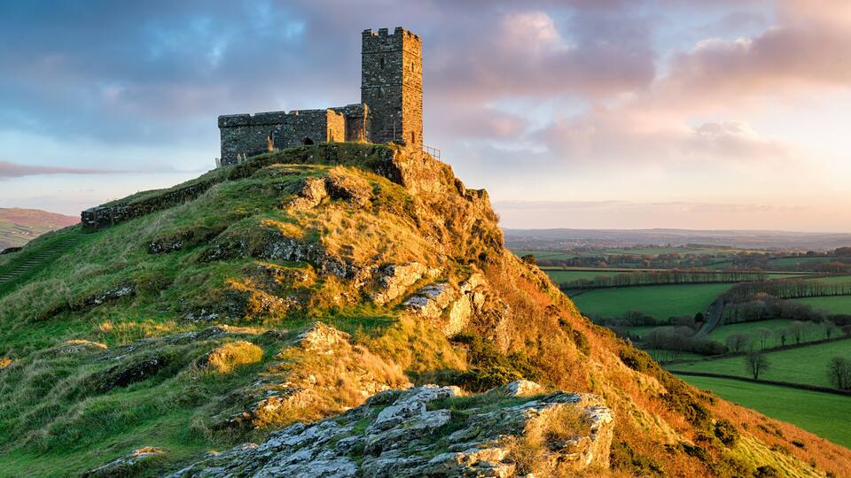 A historic stone castle on a grassy hill with a clear view of the surrounding countryside.