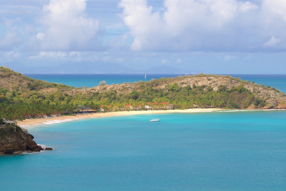 A coastal landscape with a beach, clear turquoise waters, and a small island with vegetation and buildings.