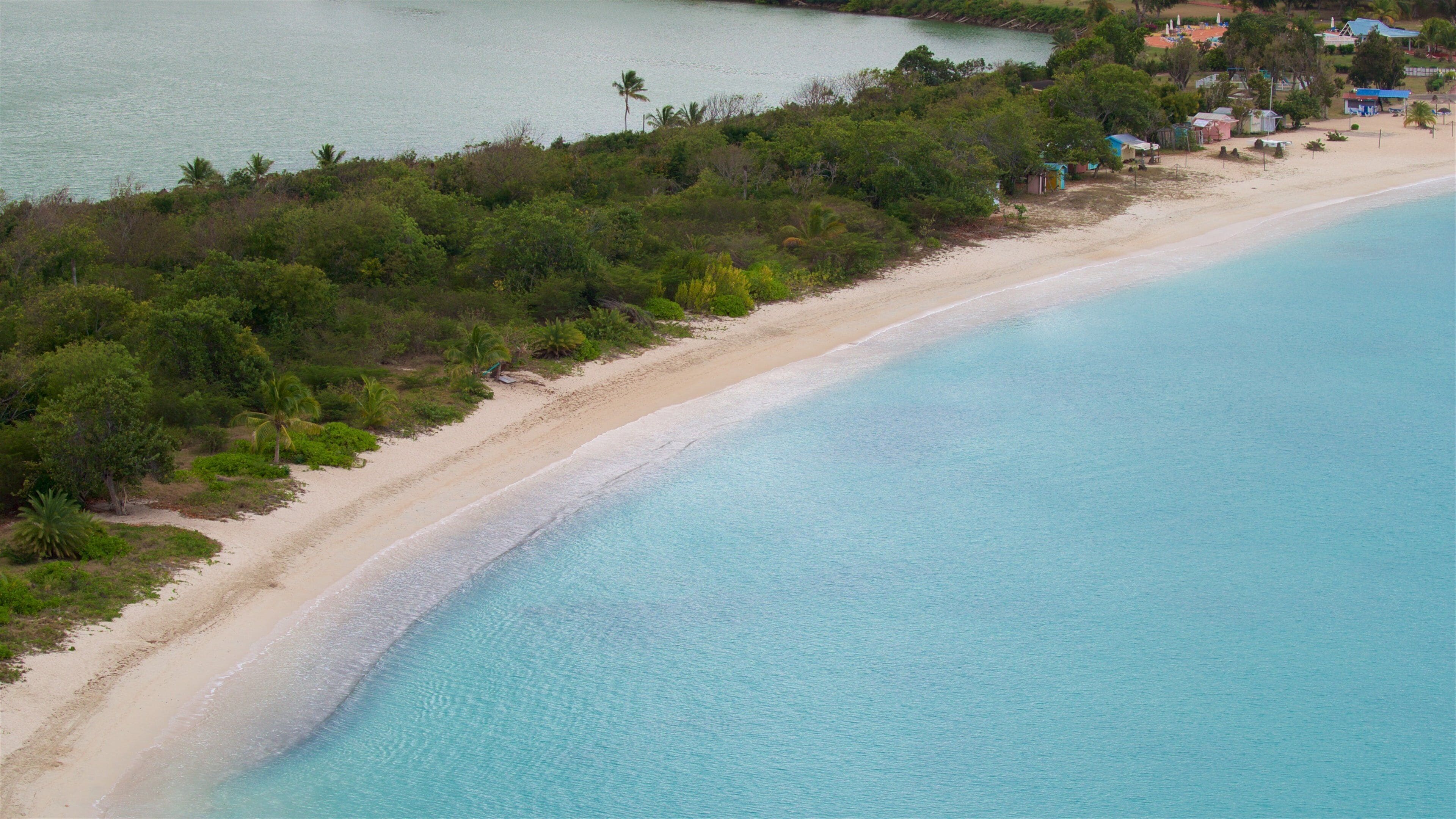 A coastal landscape with a sandy beach, clear turquoise waters, and dense greenery.