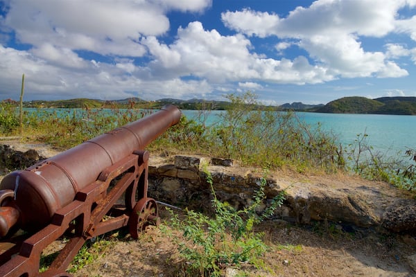 Un vieux canon rouillé, posé sur une côte rocheuse, surplombe un lac turquoise, avec des montagnes en arrière-plan.