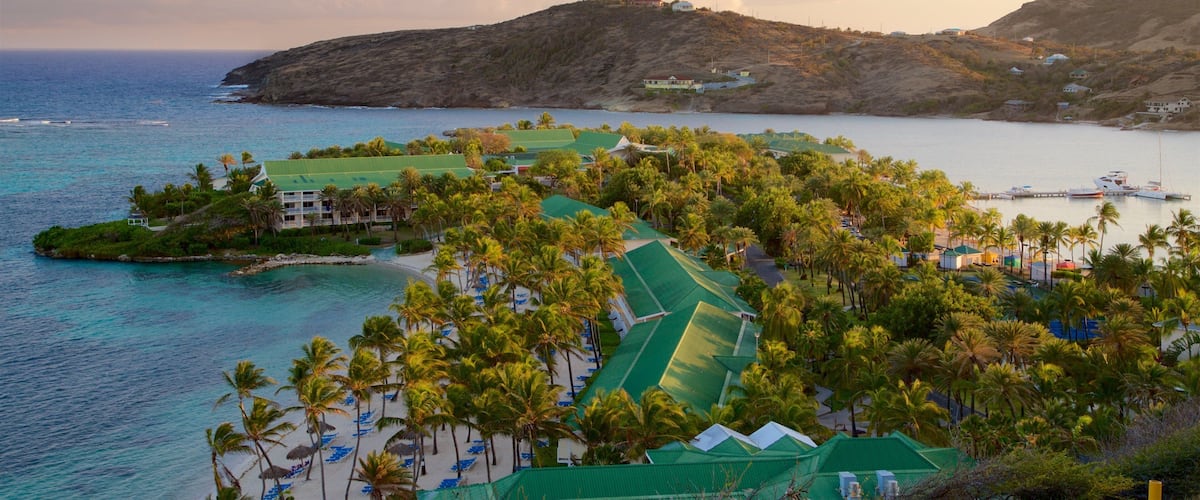 A coastal resort with palm trees, a beach, and a mountainous backdrop.