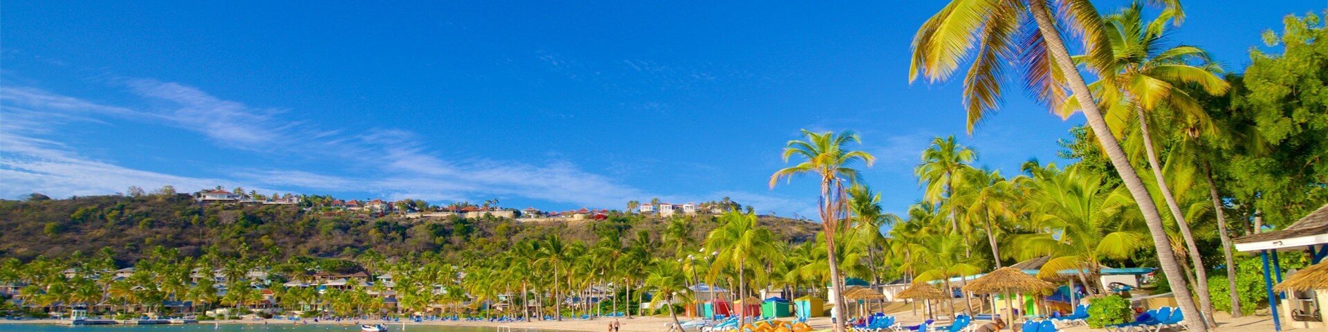 Una playa con palmeras, agua azul cristalina y una colina distante con edificios.