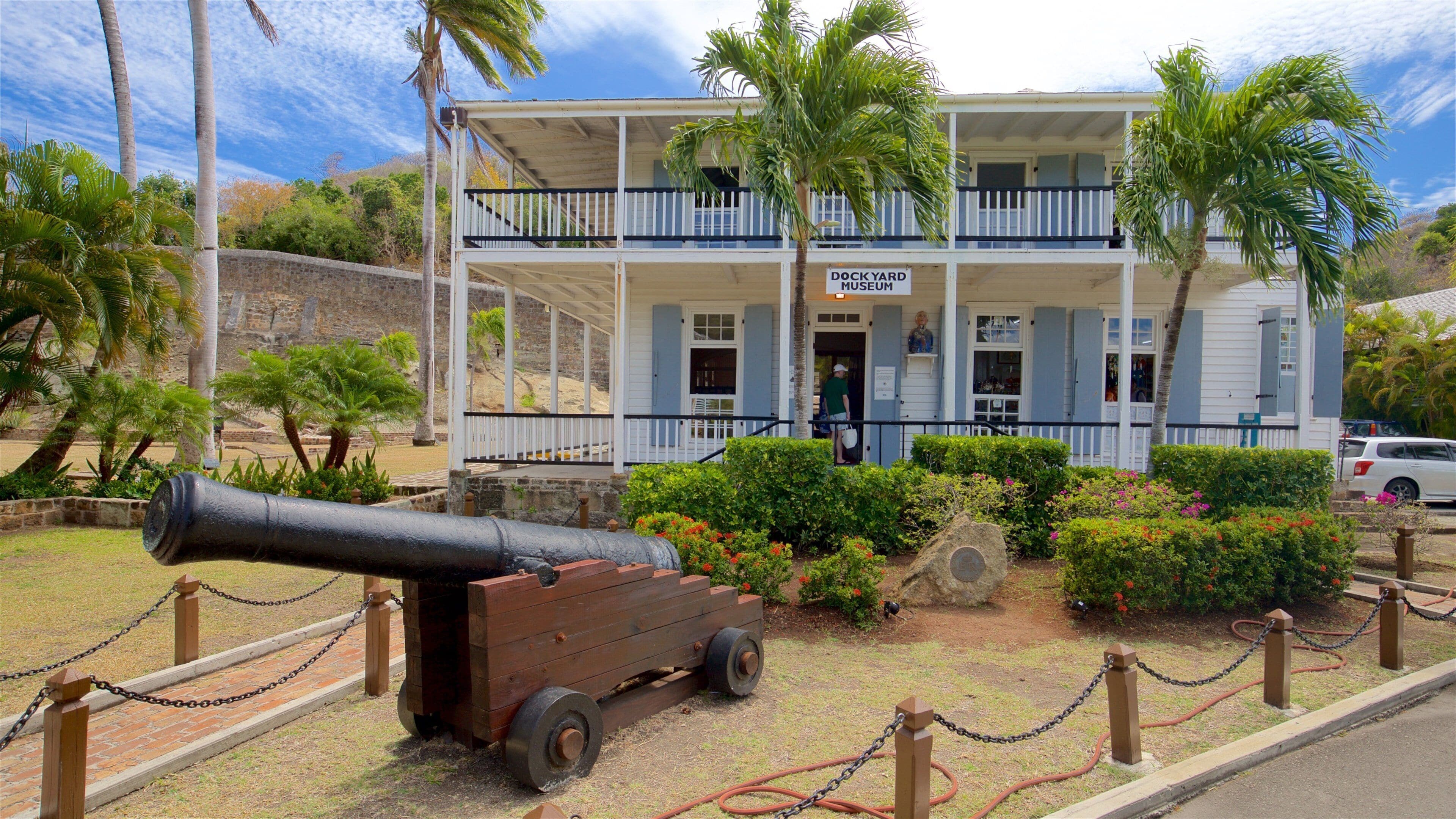 A historic building with a sign reading "Dockyard Museum" surrounded by palm trees and a cannon.