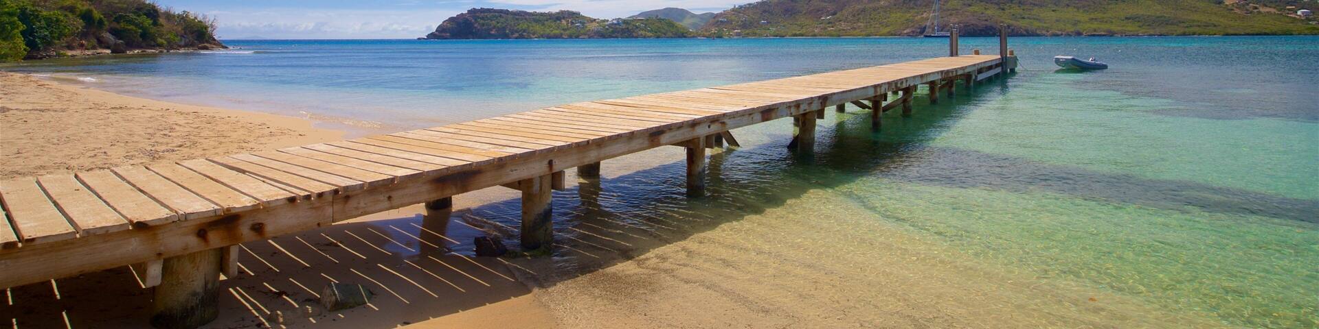 A wooden pier extending into a clear turquoise sea with a sandy beach and distant mountains.