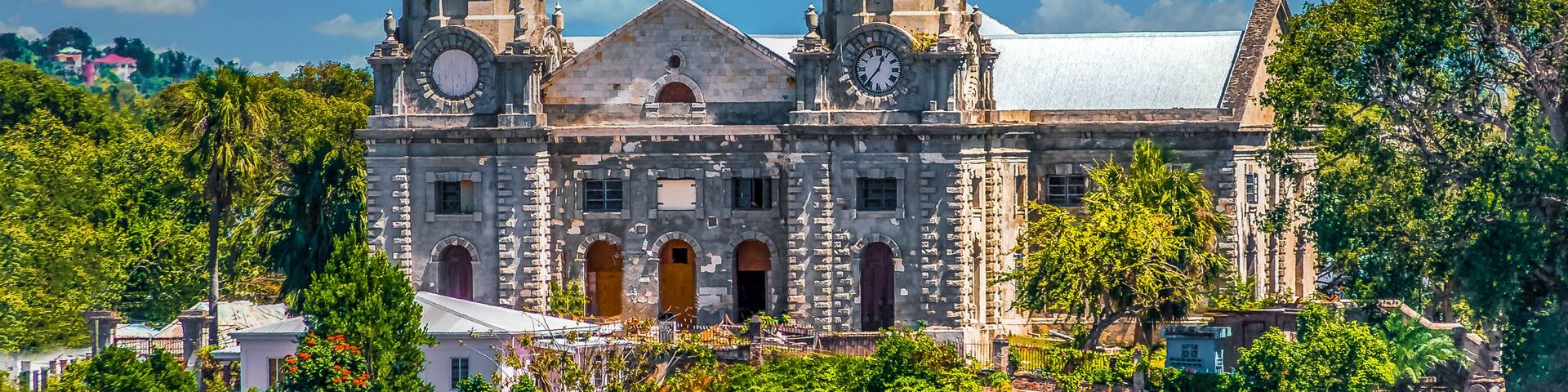 A historic church with two domed towers and a clock tower, surrounded by lush greenery.