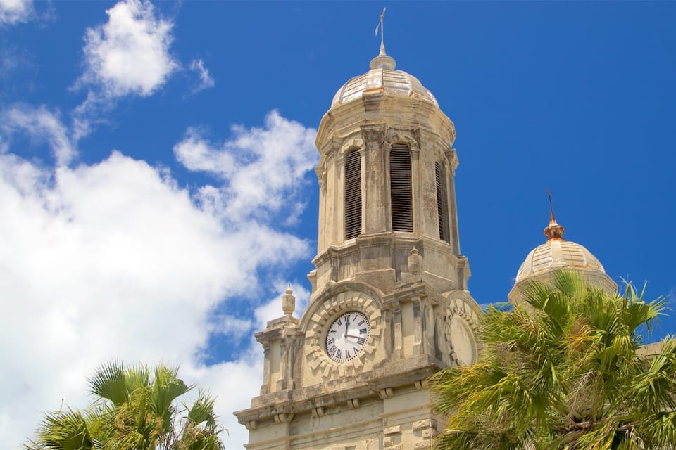 A historic building with a clock tower and domed roof under a blue sky with clouds.