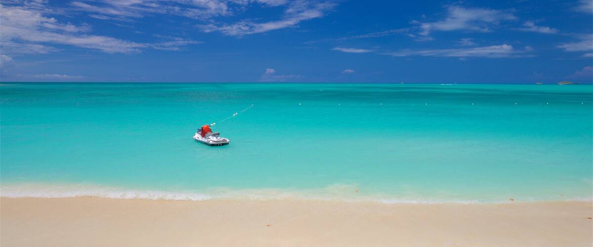 A boat on a turquoise sea with a sandy beach and a clear sky.