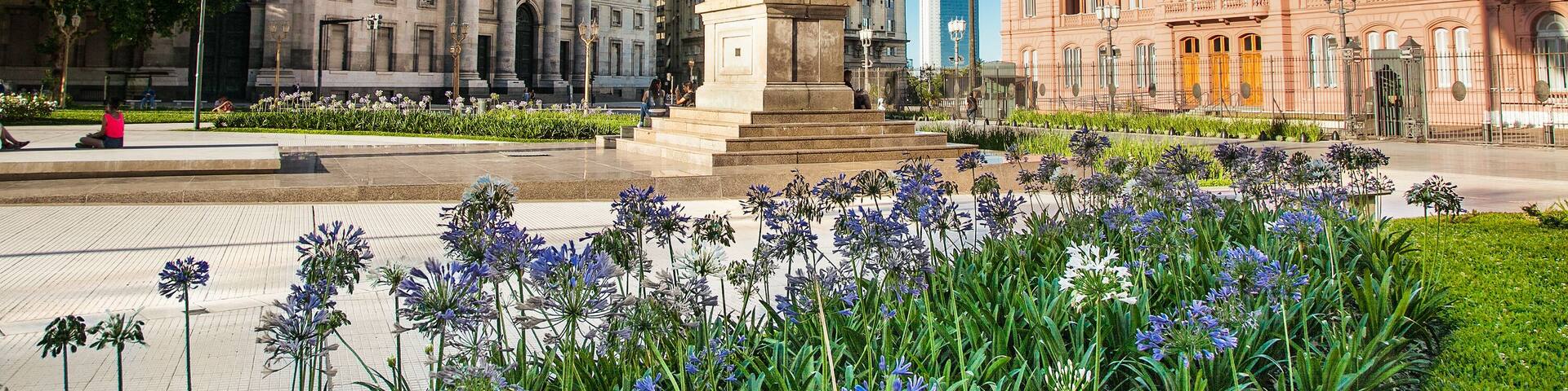 Une place centrale agrémentée d’un monument, entourée d’édifices d’architecture classique et d’un jardin fleuri.