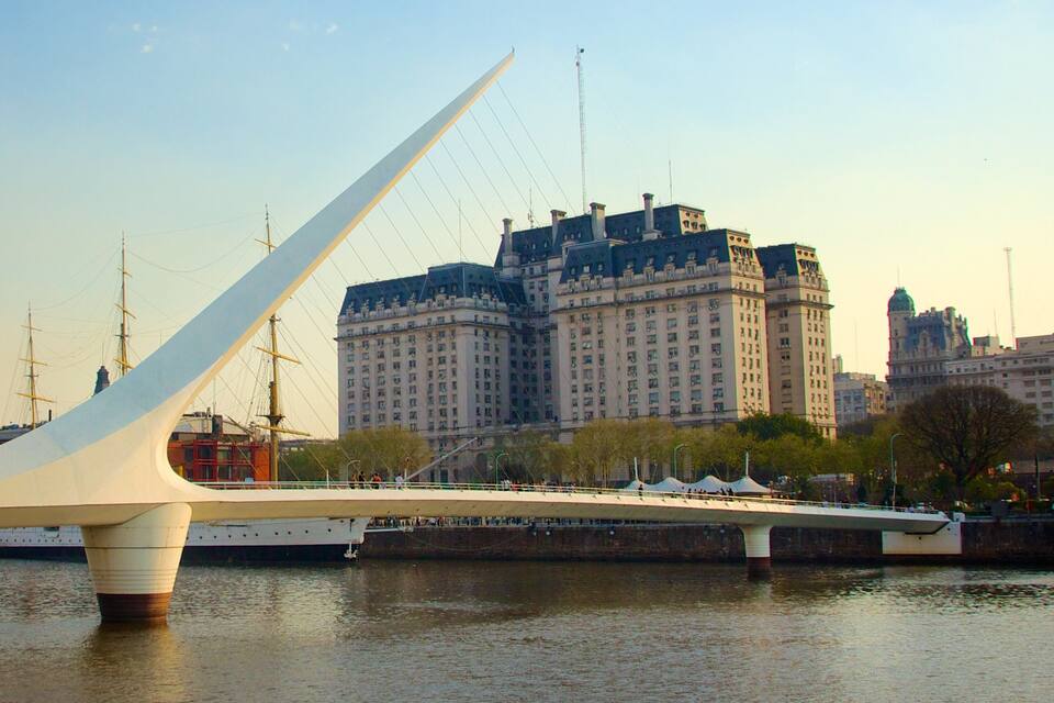 Eine moderne Brücke mit einem weißen Bogen über einem Fluss, im Hintergrund historische Gebäude.