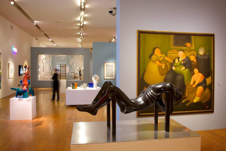 An art gallery with various artworks on display, including a sculpture on a platform and a large painting on the wall.