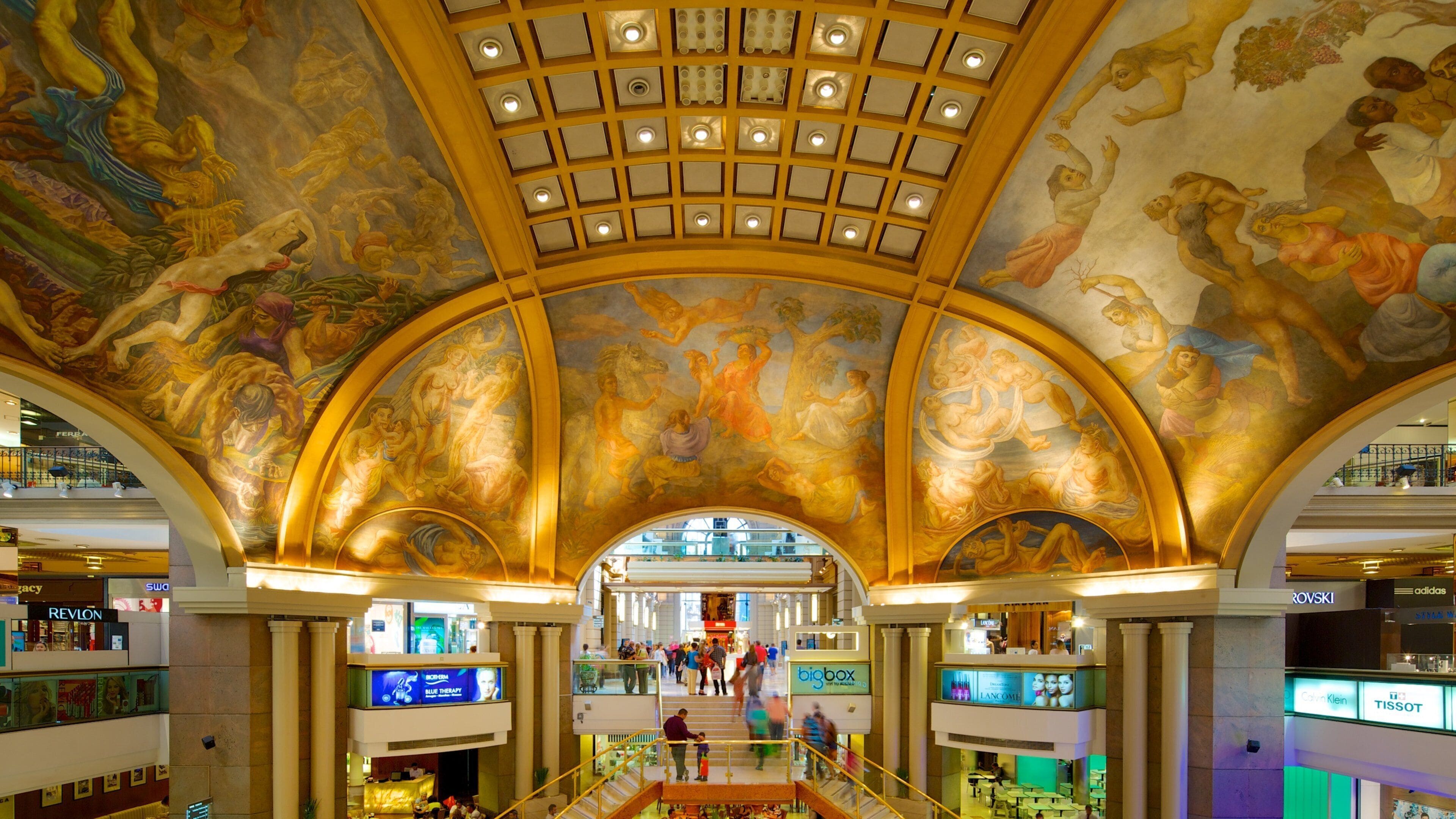 A shopping mall with a grand, arched ceiling featuring classical frescoes.
