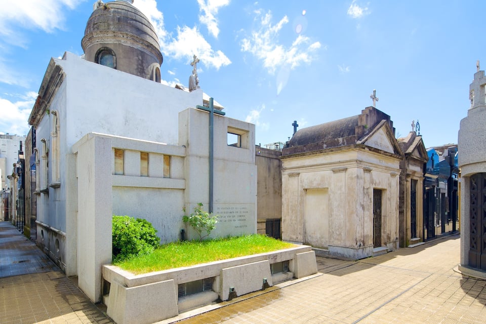 A cemetery with white tombstones, a dome-shaped building, and crosses on top.