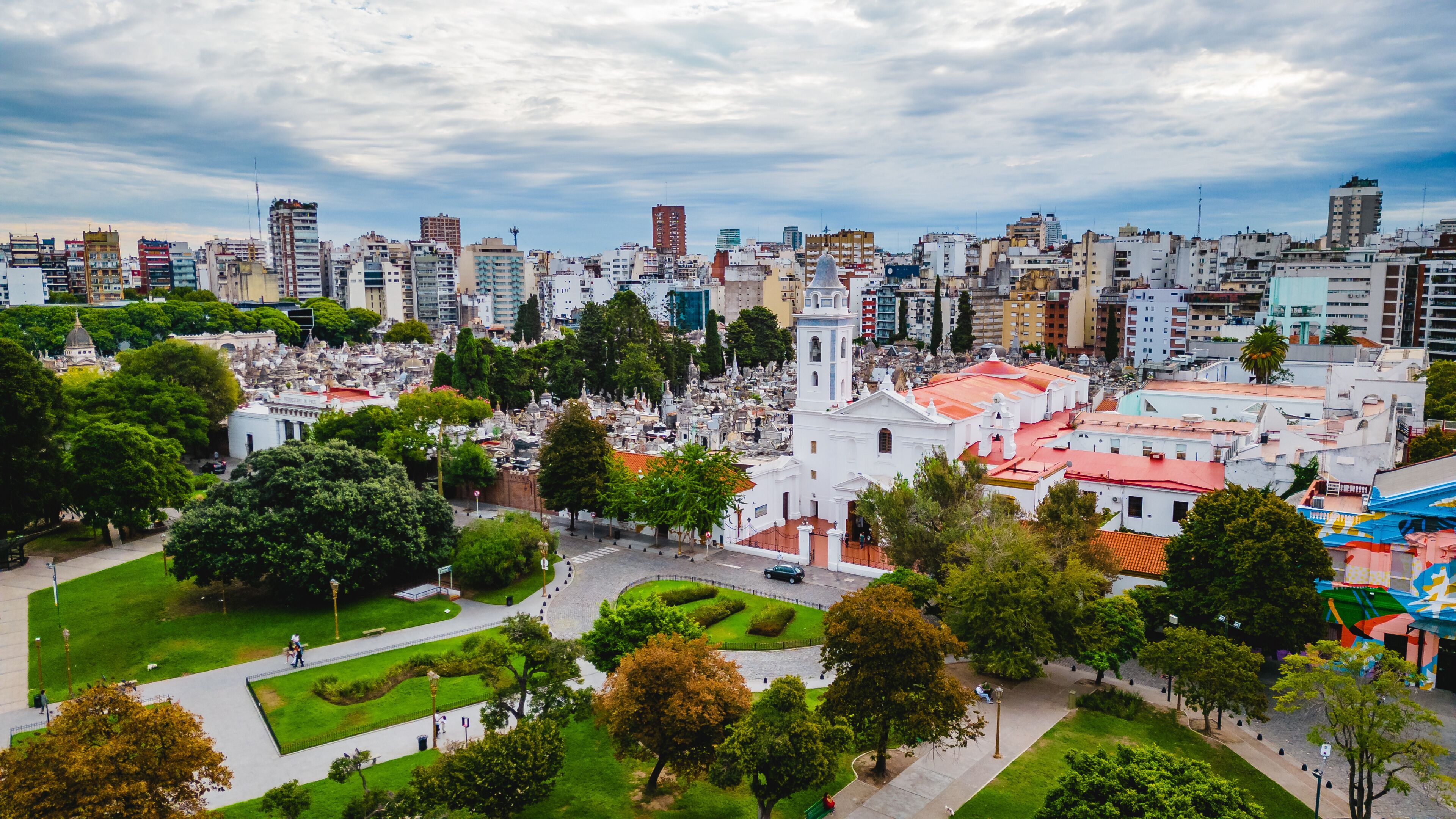 A cityscape with a prominent white church, lush green parks, and a dense urban skyline.