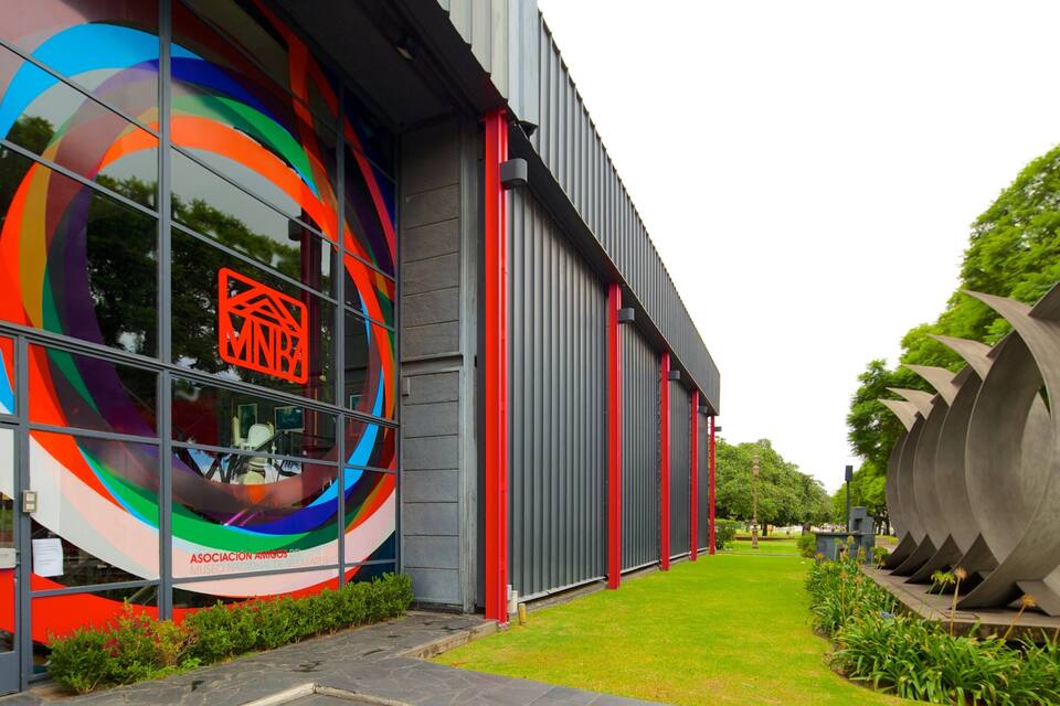 A modern building with colorful circular patterns on the facade, a large metallic sculpture, and a well-maintained garden.