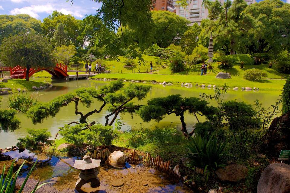 A traditional Japanese garden with a pond, rocks, and a red bridge.