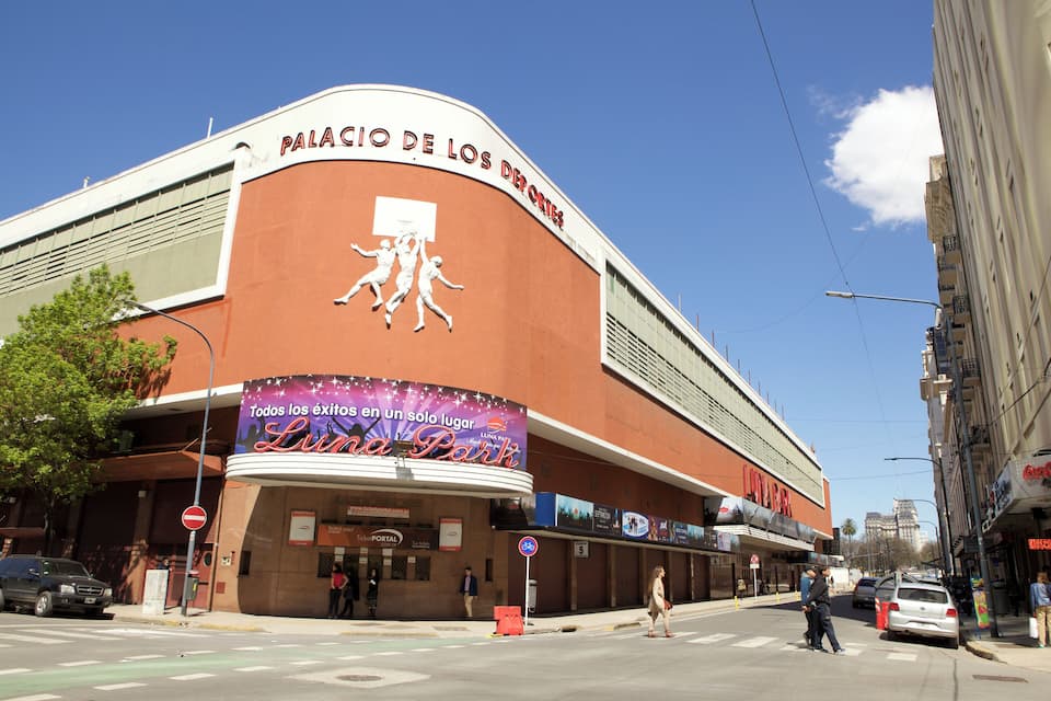 Ein großes Gebäude mit einem Schild, auf dem "Palácio de los Deportes" steht, und einem Wandgemälde von Athleten.
