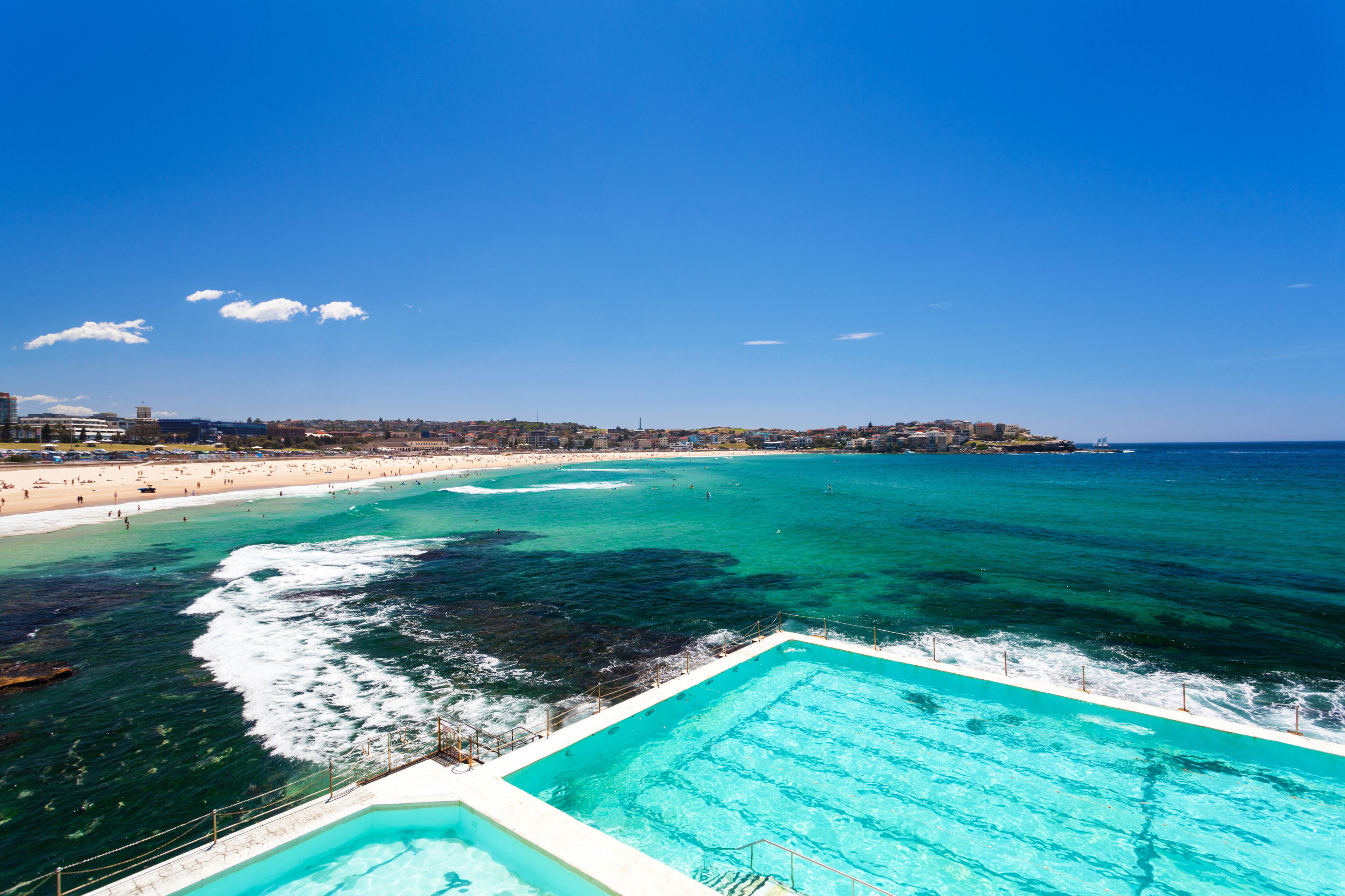 Un paisaje costero con playa, piscina y cielo azul despejado.