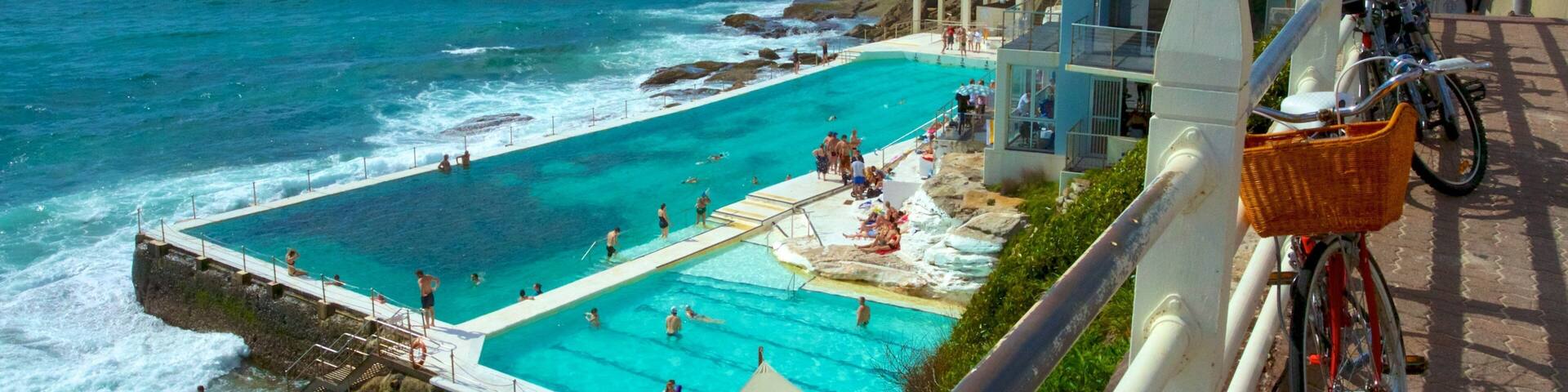 A coastal swimming pool with clear blue water, surrounded by rocky terrain and a building labeled 'Bondi Icebergs'.