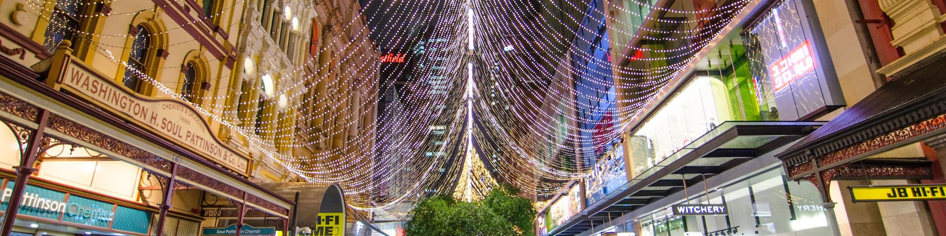 A wet street with string lights and shops.