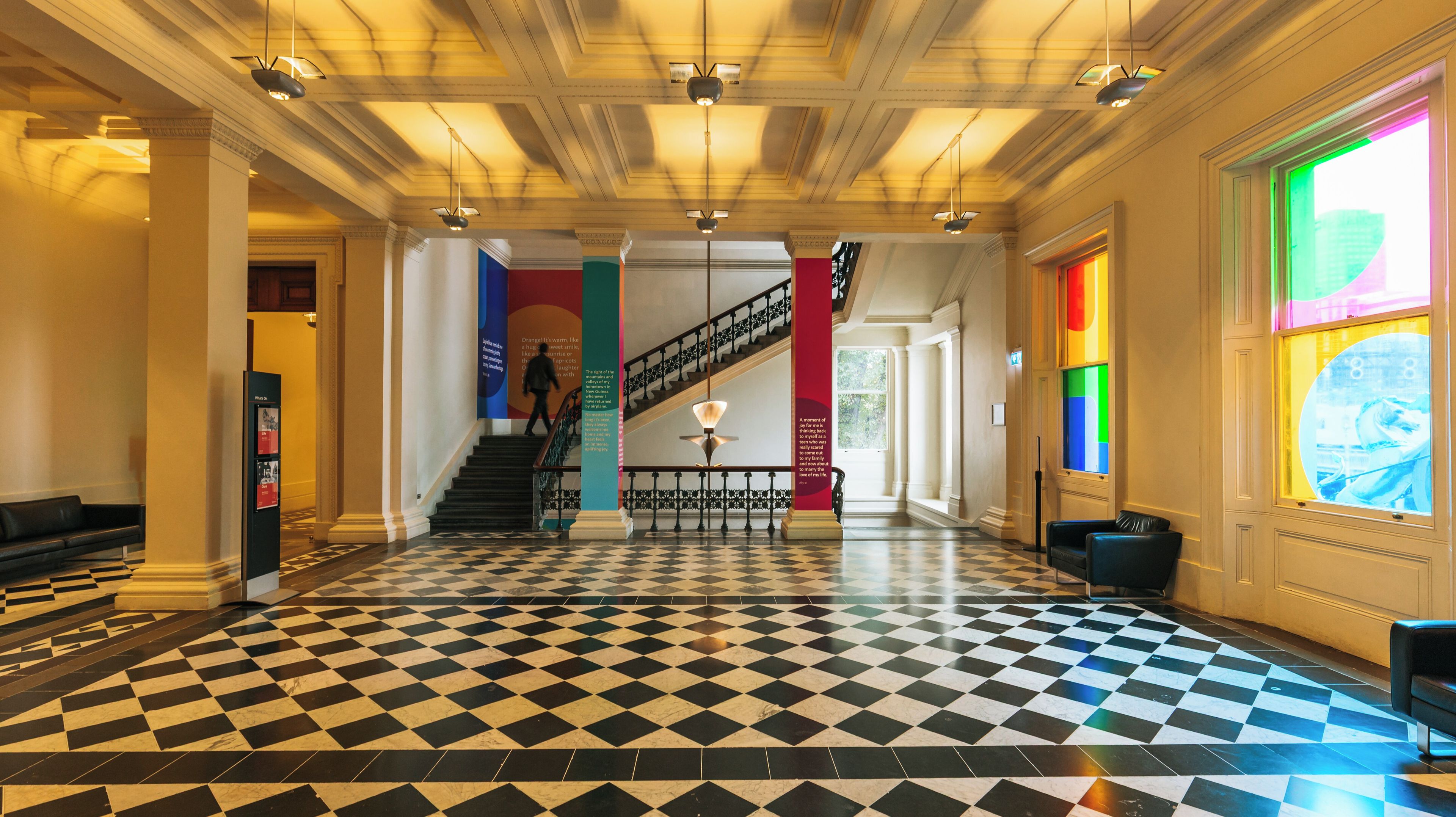 A grand lobby with a checkered floor, a staircase, and a colorful stained glass window.