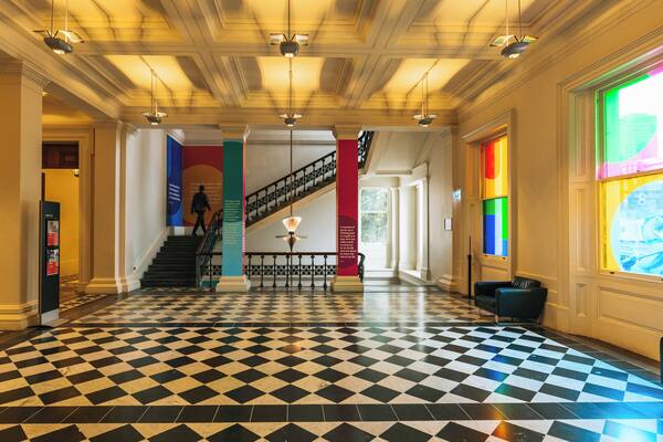 A grand lobby with a checkered floor, a staircase, and a colorful stained glass window.