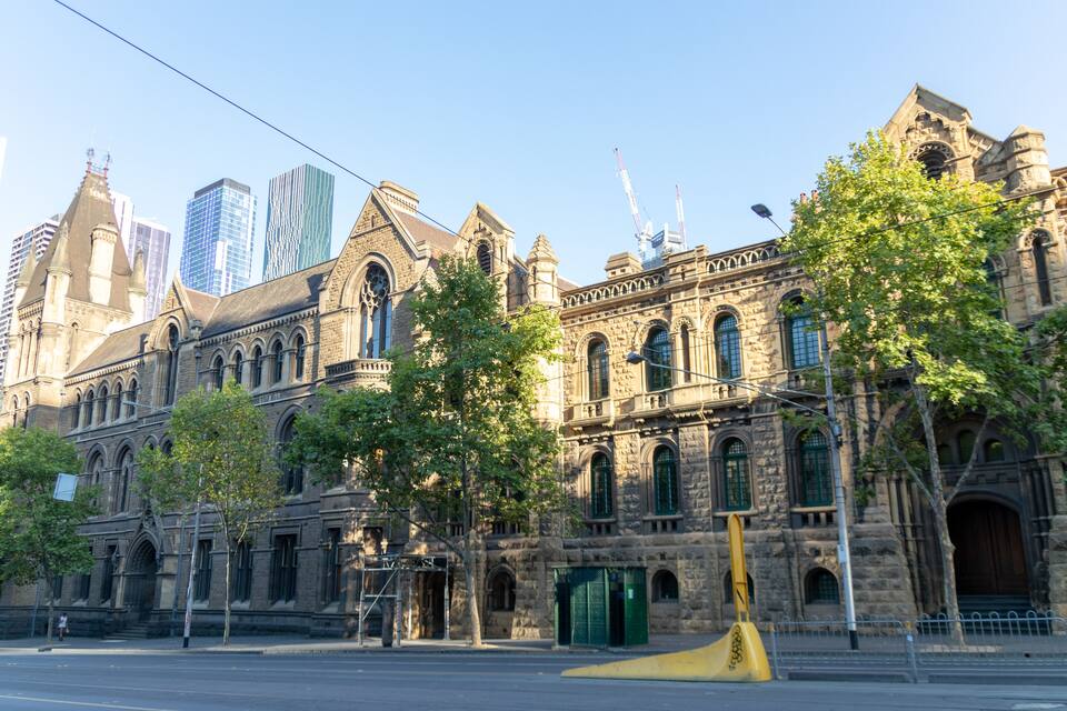 Un edificio histórico con arquitectura ornamentada, rodeado de rascacielos modernos y árboles.