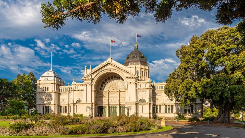 A large, ornate building with a prominent dome and two flagpoles, surrounded by lush greenery.