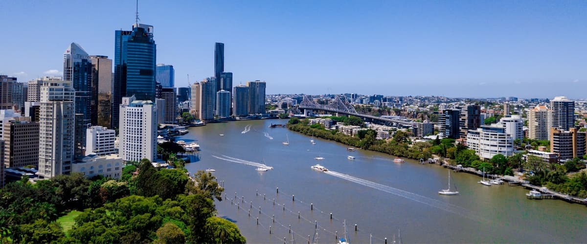 A city skyline with modern skyscrapers, a river with boats, and green areas along the riverbanks.