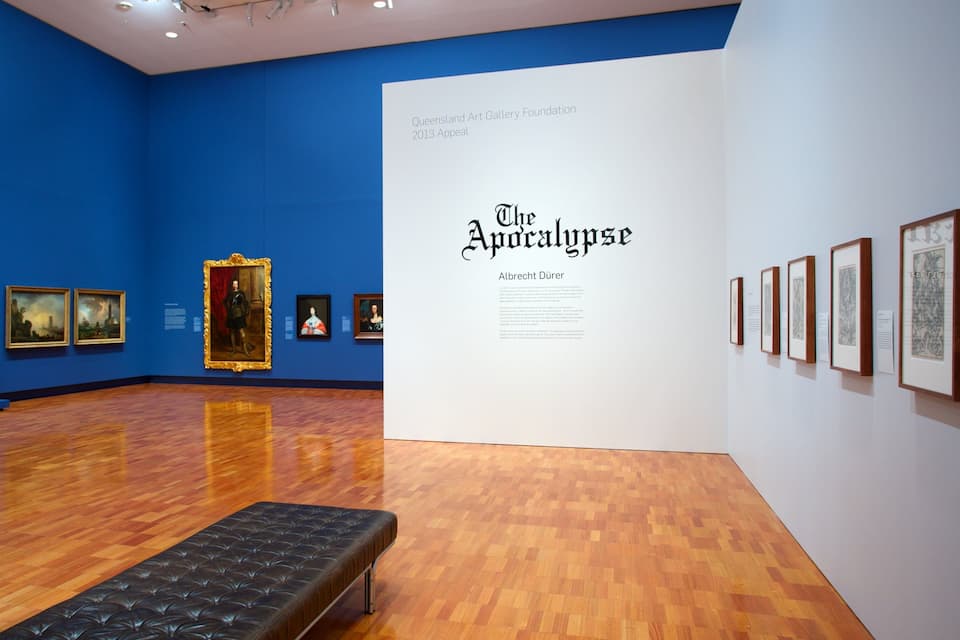 An art gallery with blue walls, wooden floors, and various framed artworks.