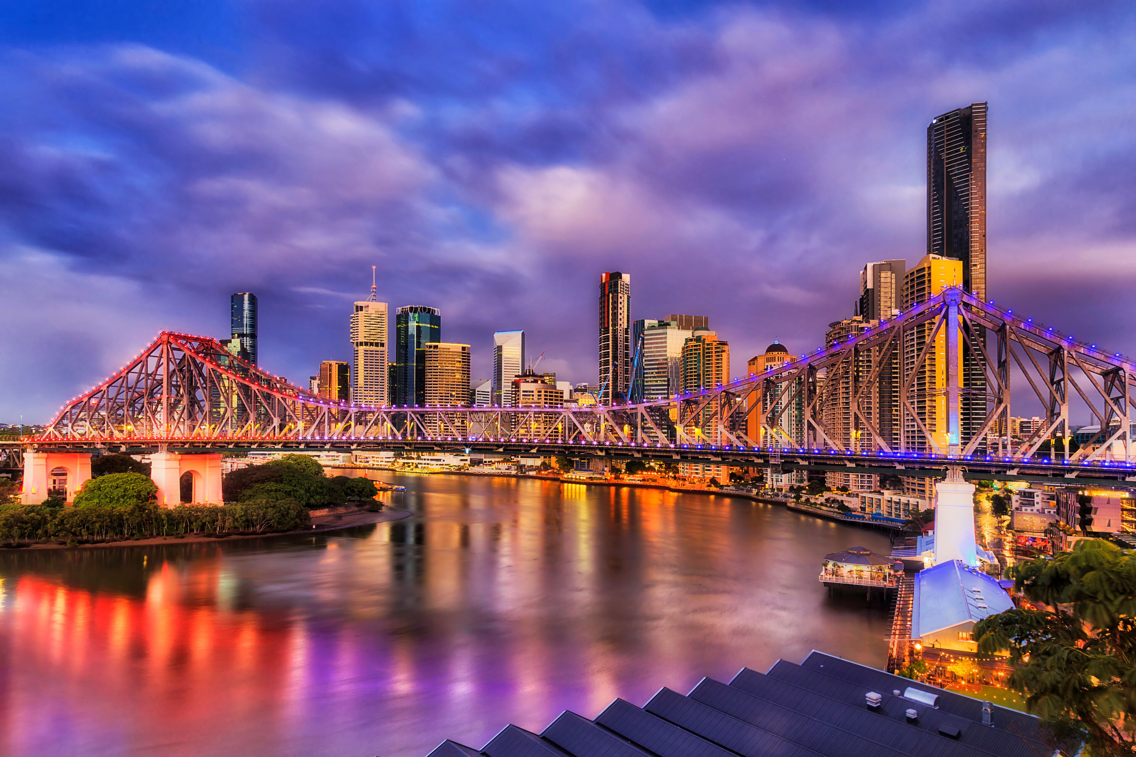 A city skyline with modern skyscrapers, a prominent red bridge, and a calm river reflecting the structures.